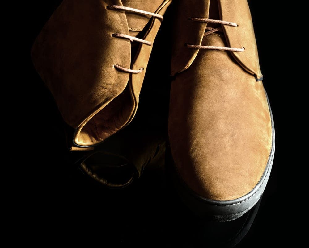 A pair of brown suede shoes on a dark reflective surface